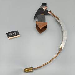 Foto van een metalen en beschilderde figuur van een tuimelman met een lange zaag.